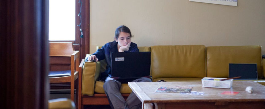 Teen member sitting on couch working on a laptop
